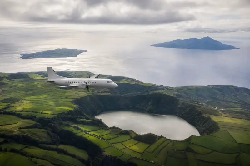 Turbo-hélice regional a sobrevoar campos verdes e uma lagoa vulcânica nos Açores